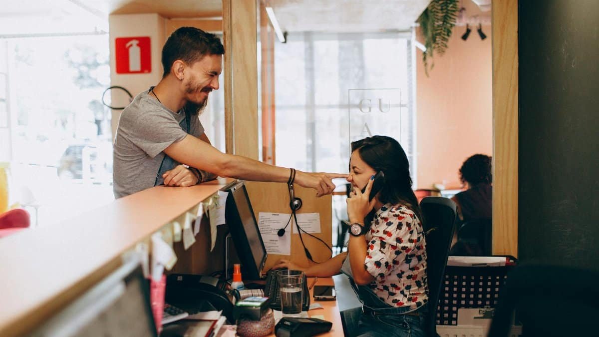 A man playfully interacts with a woman at a reception desk in a lively and modern office setting.