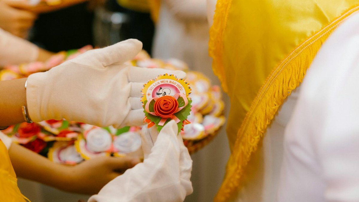 Gloved hands exchanging a decorative badge during a cultural ceremony indoors.