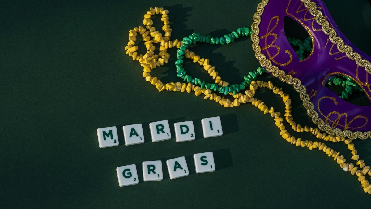 Colorful Mardi Gras mask and beads on green background, perfect for carnival themes.