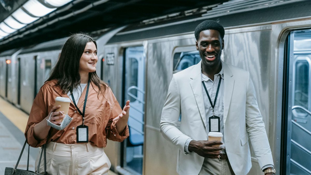 Two professionals conversing and holding coffee at an urban subway platform.