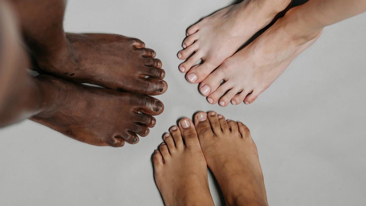 Close-up of diverse feet standing together on a neutral surface, symbolizing unity.