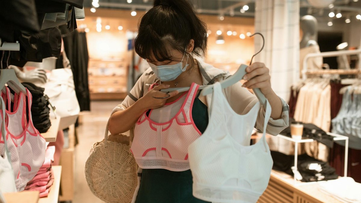 Woman wearing a mask choosing sports bras in a store during pandemic times.
