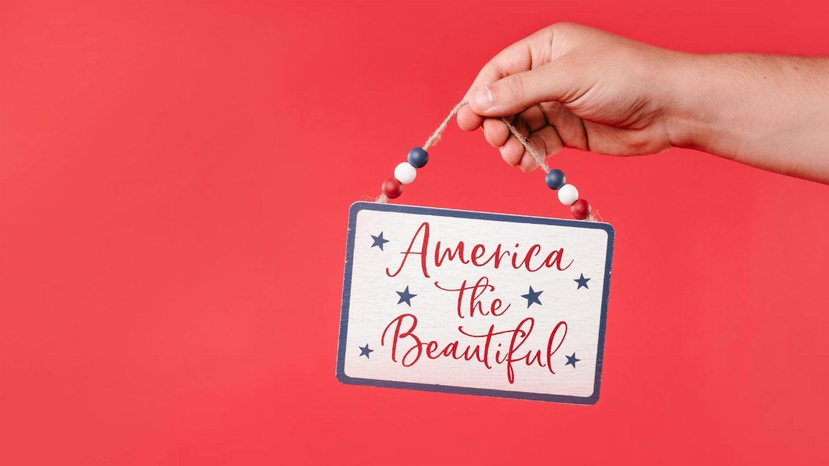 A hand holds a decorative patriotic sign on a vibrant red background.