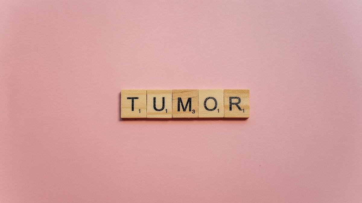 Wooden letter tiles spelling 'tumor' arranged on a pink background for healthcare themes.