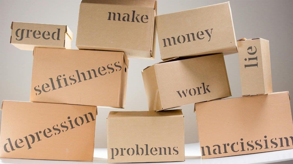 Stacked cardboard boxes displaying words like greed, depression, and problems, highlighting mental health themes.