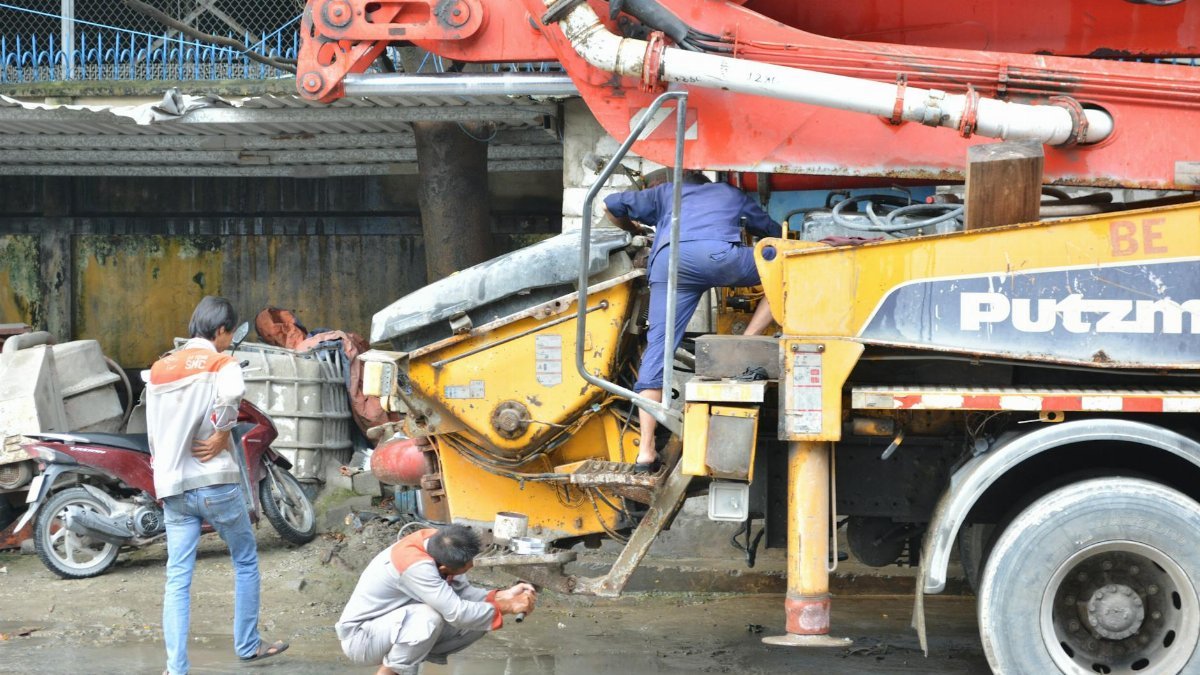Construction workers fixing a cement mixer truck outdoors, showcasing teamwork and machinery maintenance.
