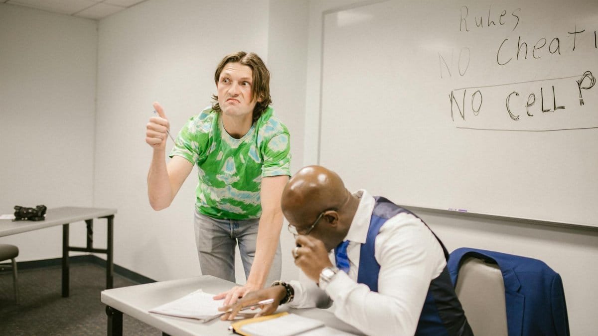 A teacher catches a student attempting to cheat with a hand signal during a classroom exam.