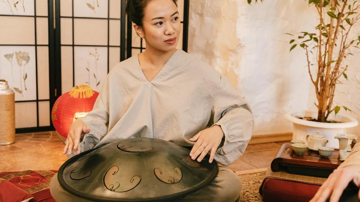 An Asian woman playing a steel tongue drum in a cozy indoor setting. Peaceful and cultural ambiance.