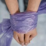 Hands bound with purple plastic in a close-up view conveying restriction and bondage.