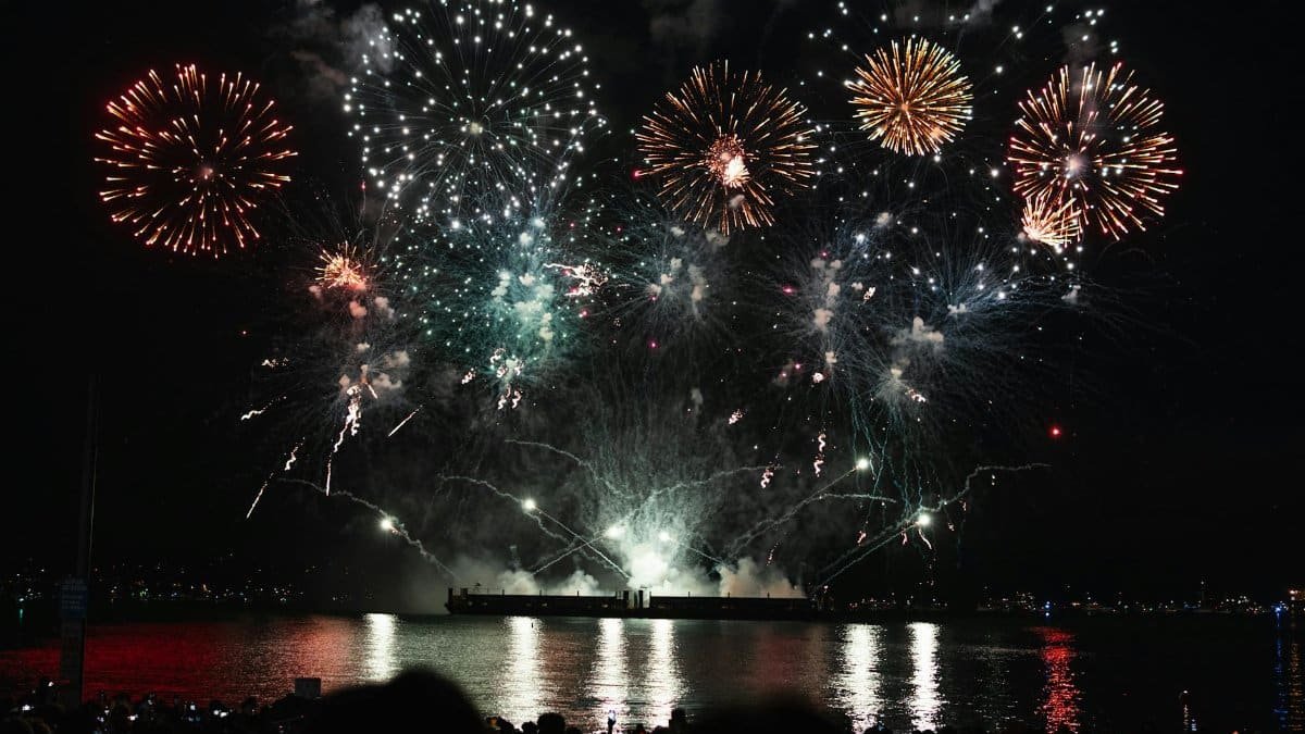 Dazzling fireworks display over Vancouver's waterfront at night, reflecting on the water.