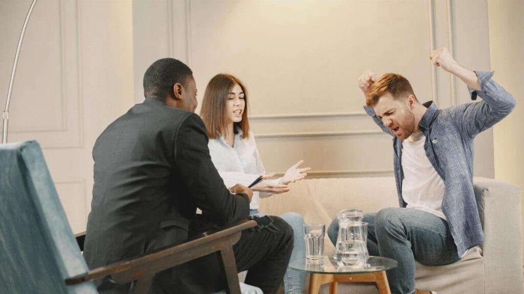 A couple engaging in a heated discussion during a therapy session with a therapist.