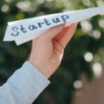 Close-up of a hand holding a paper plane with 'Startup' written, symbolizing a business launch.
