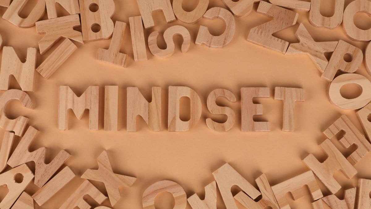 Wooden alphabet letters arranged to spell 'Mindset' on a peach background.