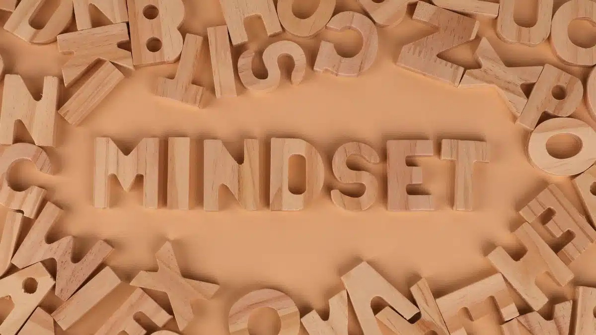Wooden alphabet letters arranged to spell 'Mindset' on a peach background.