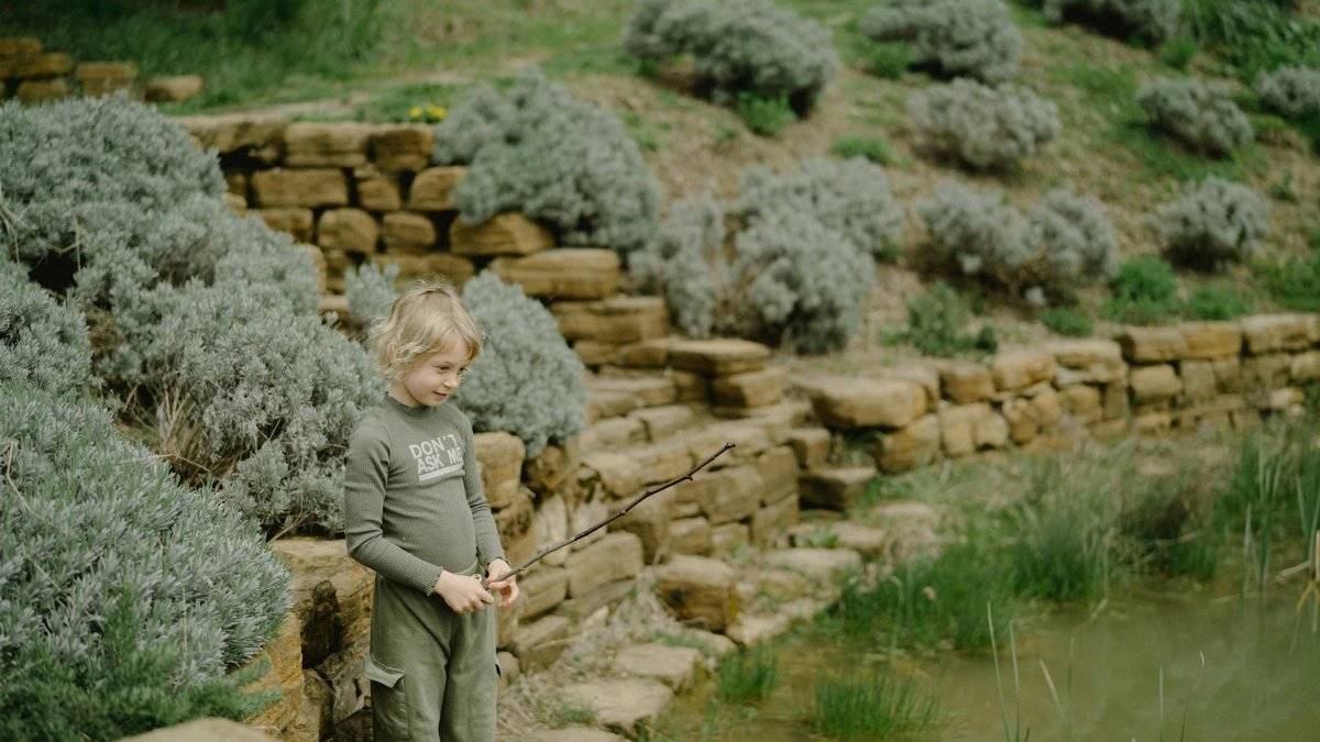 Cute child standing by a pond with a stick, exploring nature's serenity.