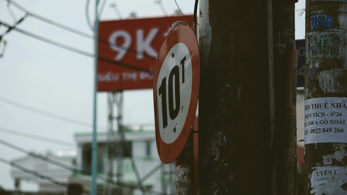 Urban street scene featuring a weathered 10t weight limit sign, with wires and poles.