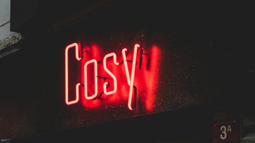 Glowing red neon 'Cosy' sign illuminating a dark urban street corner at night.