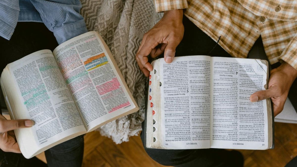 Two adults reading religious texts with highlighted passages indoors, sharing a moment of learning and connection.