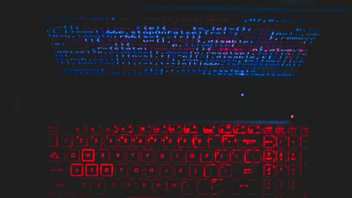Dark-themed laptop setup with a red glowing keyboard and code on screen, ideal for tech enthusiasts.