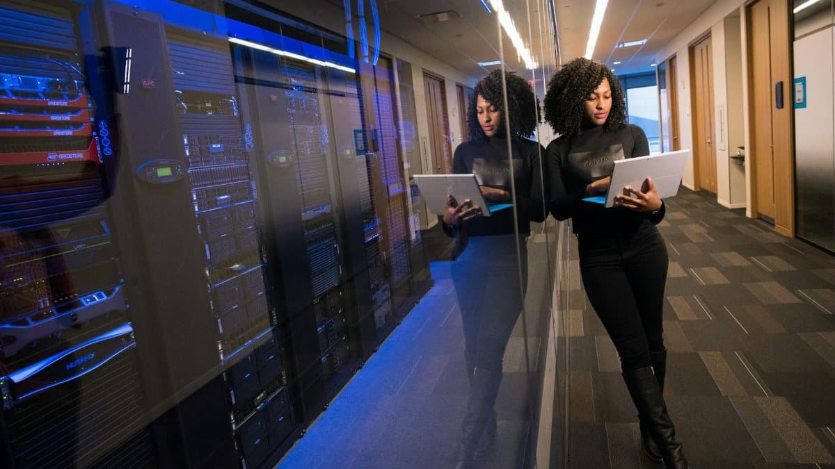 A woman using a laptop navigating a contemporary data center with mirrored servers.