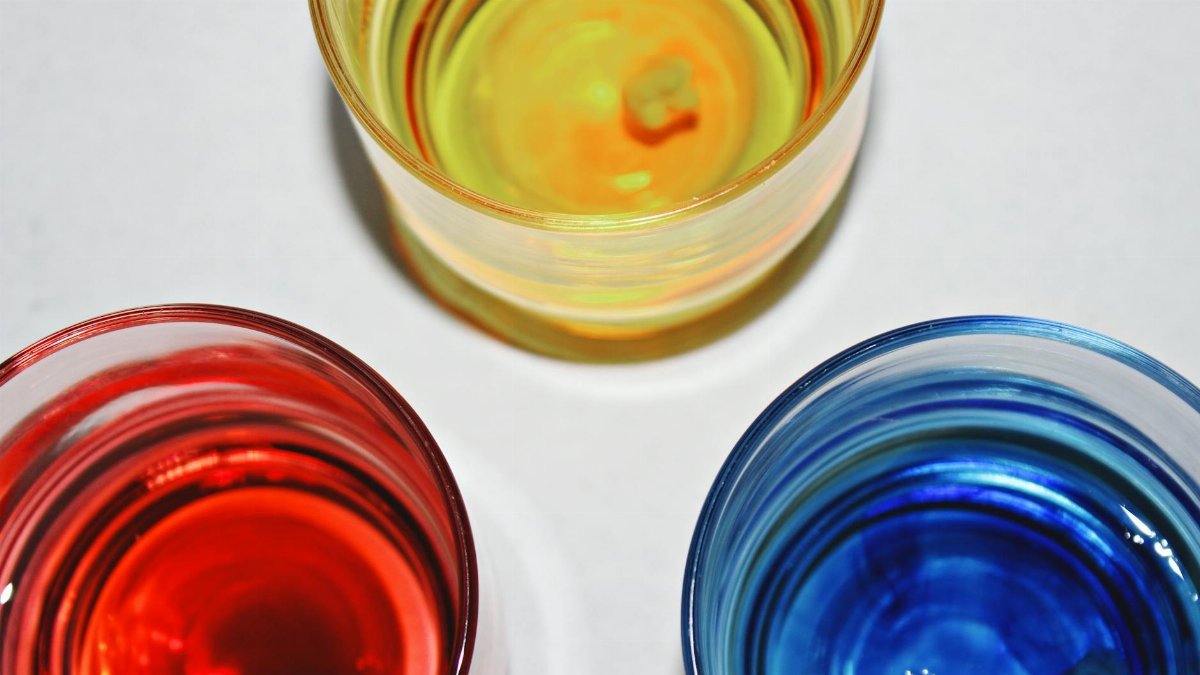 Top view of three vibrant glasses filled with different colored water on a white background.