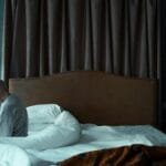 A senior man in pajamas sits on a bed, conveying solitude and reflection in a dark room.