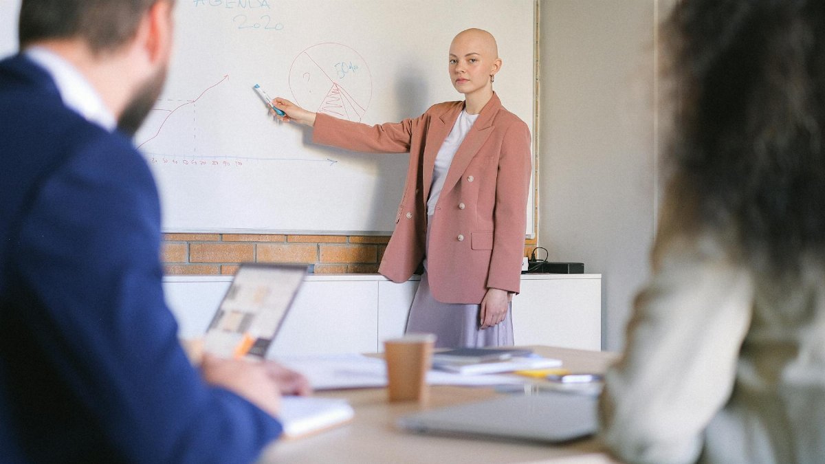 Confident businesswoman presenting data to colleagues on a whiteboard in a professional office setting.