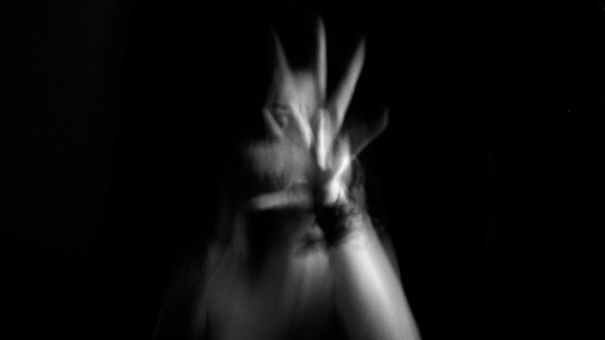Artistic black and white image of a blurred hand reaching out, creating a spooky abstract effect.