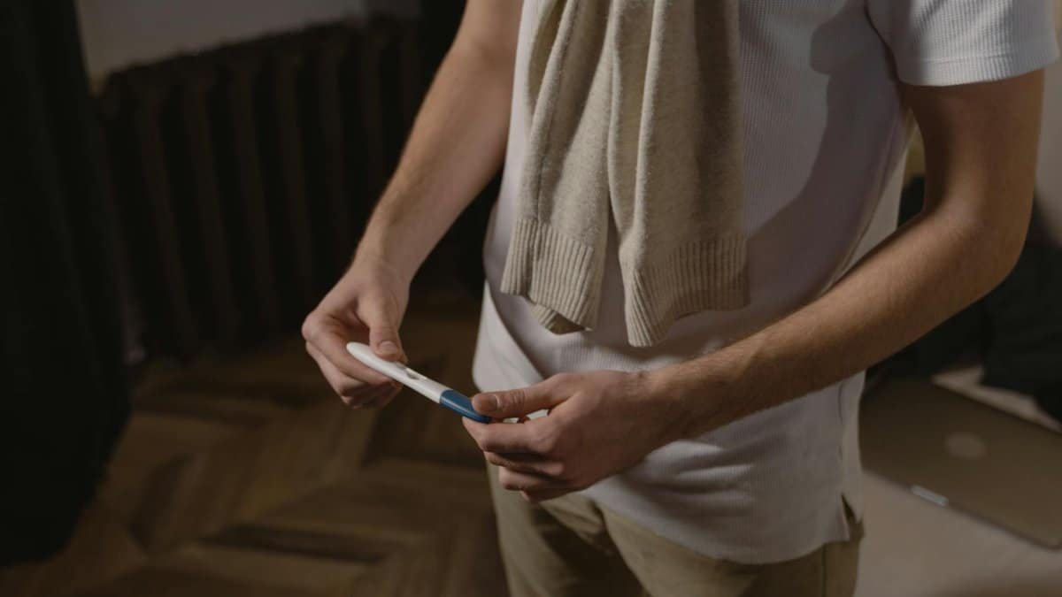 A man in casual attire examining a pregnancy test indoors.