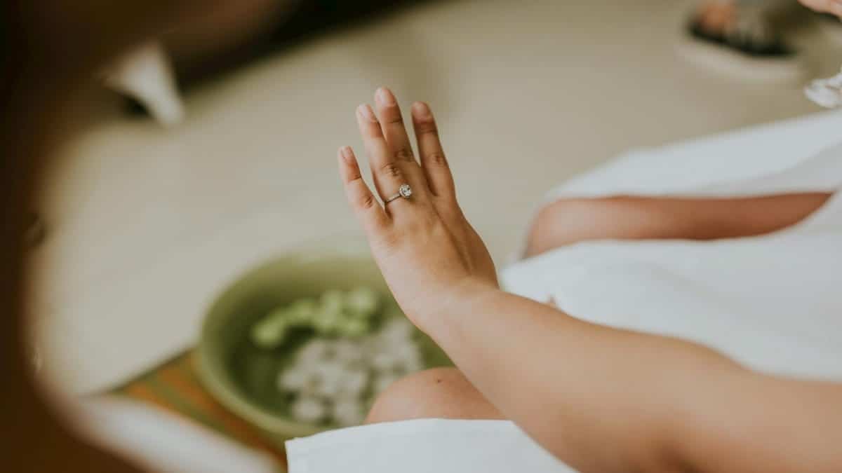 A close-up of a woman's hand adorned with a diamond engagement ring, captured indoors.