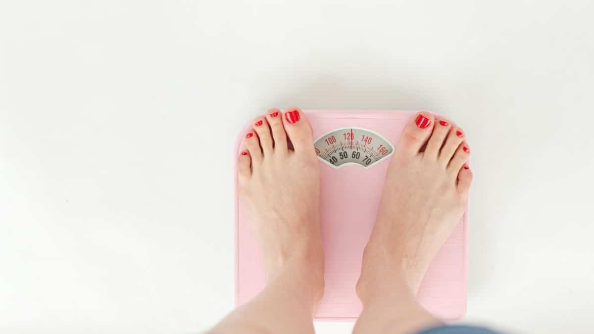 Top view of crop anonymous barefoot female measuring weight on scales on white background