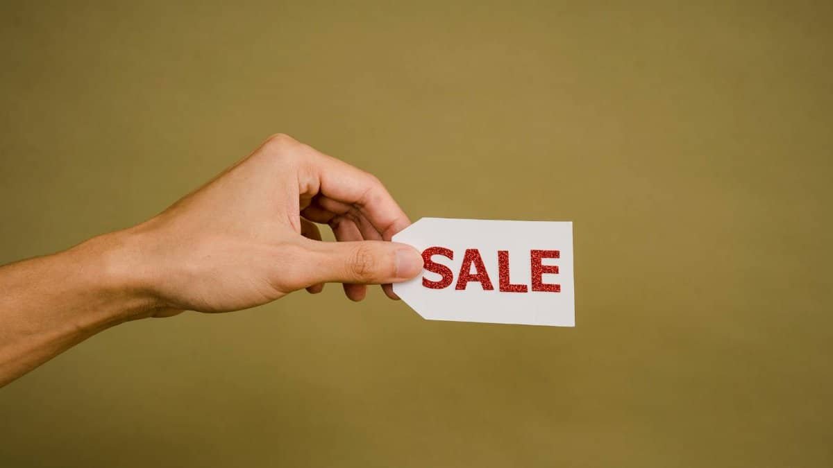 A hand holding a 'SALE' tag on a brown background, perfect for retail promotion.