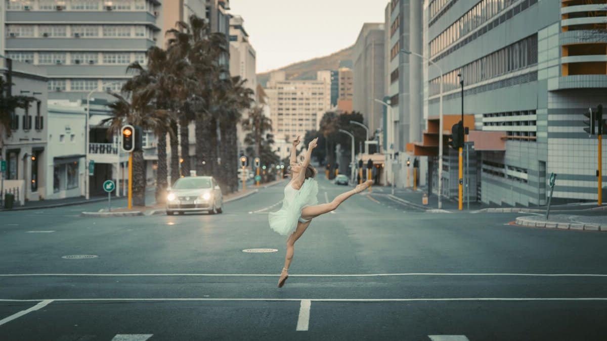 Graceful ballet dancer performing a leap on an empty street at dawn, surrounded by urban architecture.