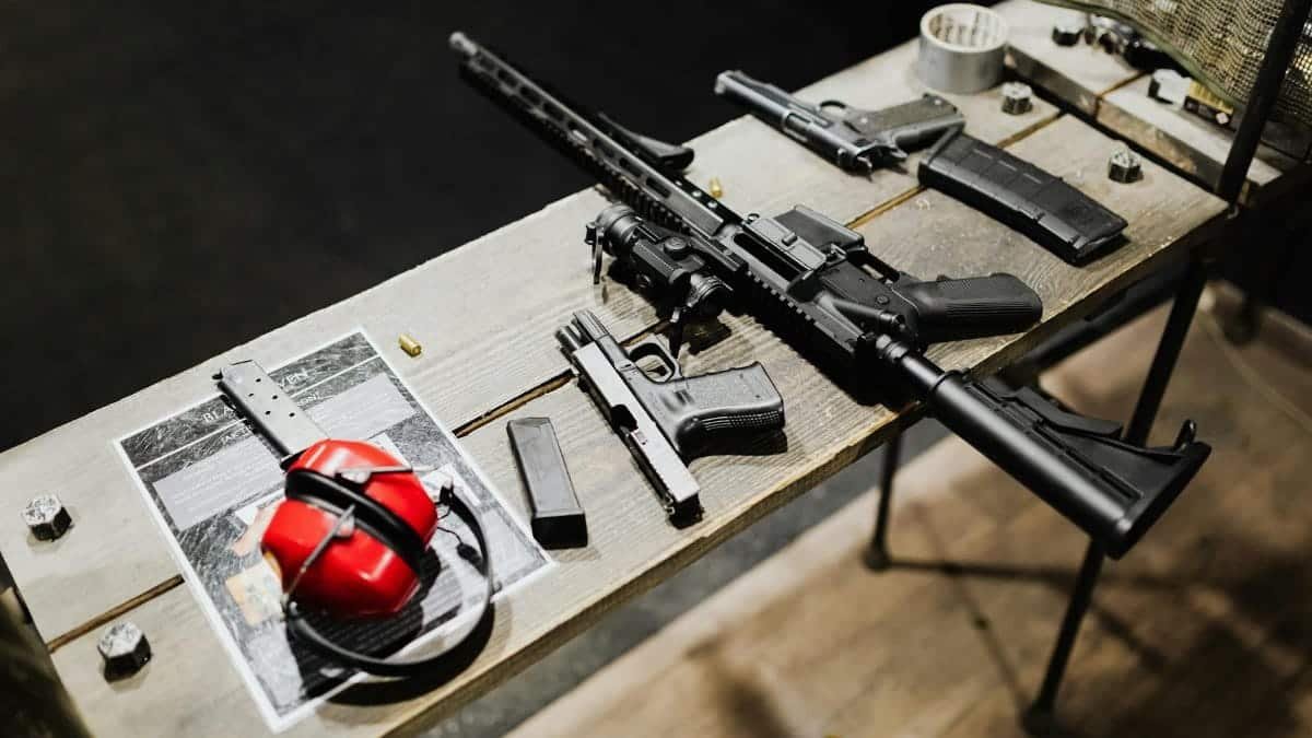A variety of guns and accessories displayed on a wooden table indoors, featuring ear protection.