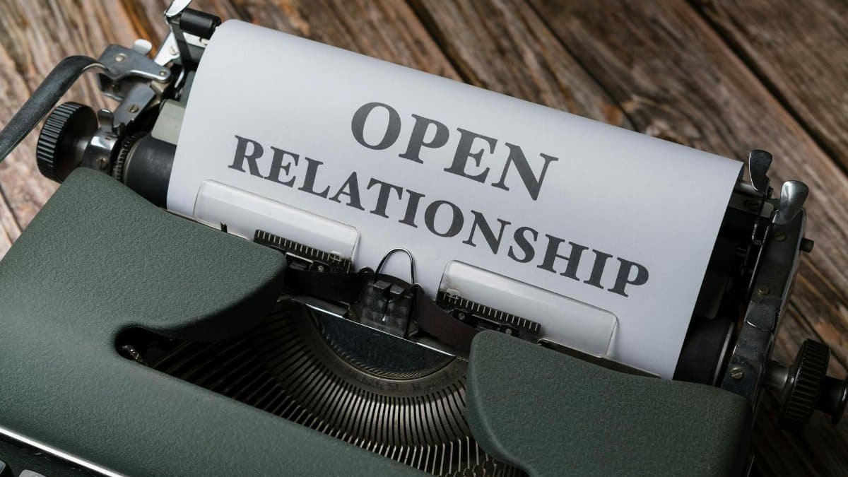 A vintage typewriter displaying the typed words 'Open Relationship' over a wooden background.