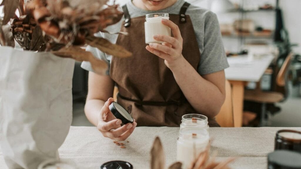 A woman crafting candles in a rustic workshop, focusing on scents and quality.