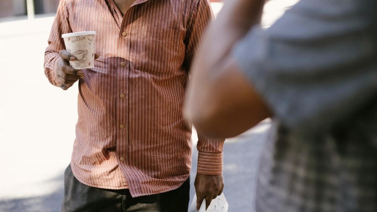 Two men enjoy a casual coffee break on a sunny urban street, engaging in conversation.