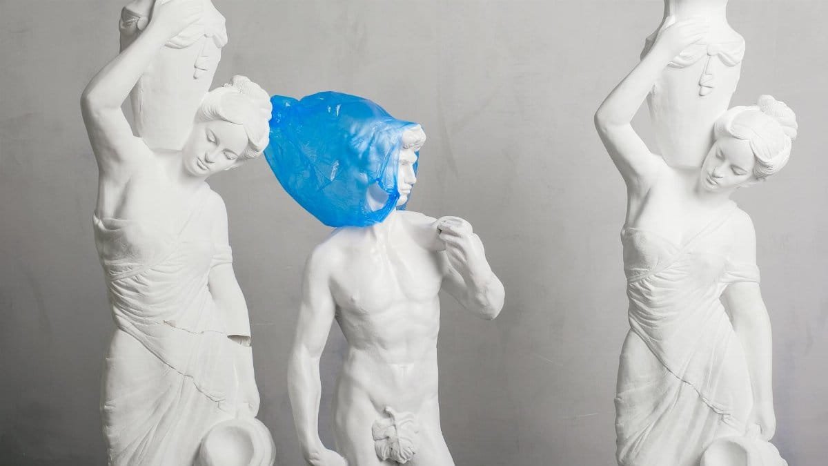 Greek marble statues adorned with a contrasting blue plastic bag conveying environmental themes.
