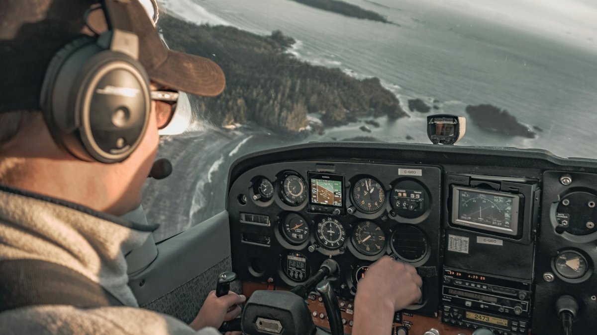 Pilot in cockpit flying over a coastal landscape, showcasing the control panel and ocean view.