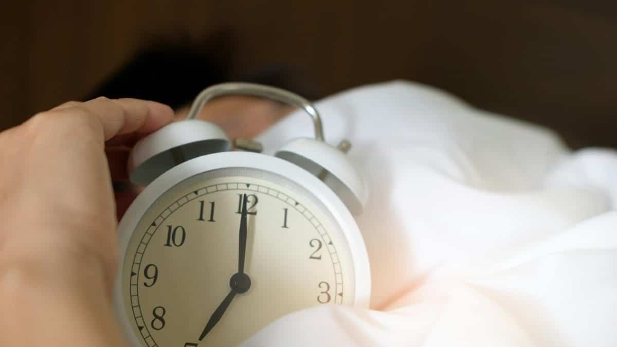 A close-up of a hand reaching for a ringing alarm clock, symbolizing waking up in the morning.
