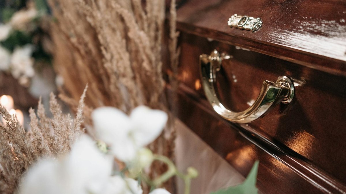 Close-up of a polished wooden casket adorned with floral arrangements, symbolizing loss and remembrance.