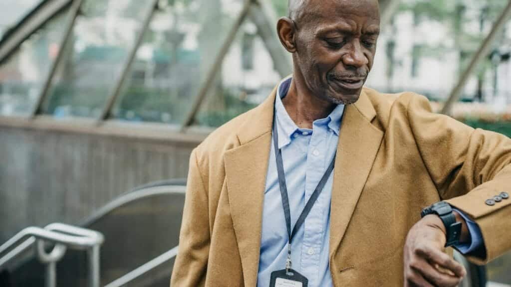Crop punctual African American male in elegant formal clothes standing near metro entrance and checking time on wristwatch