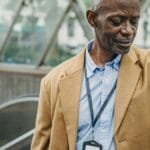 Crop punctual African American male in elegant formal clothes standing near metro entrance and checking time on wristwatch