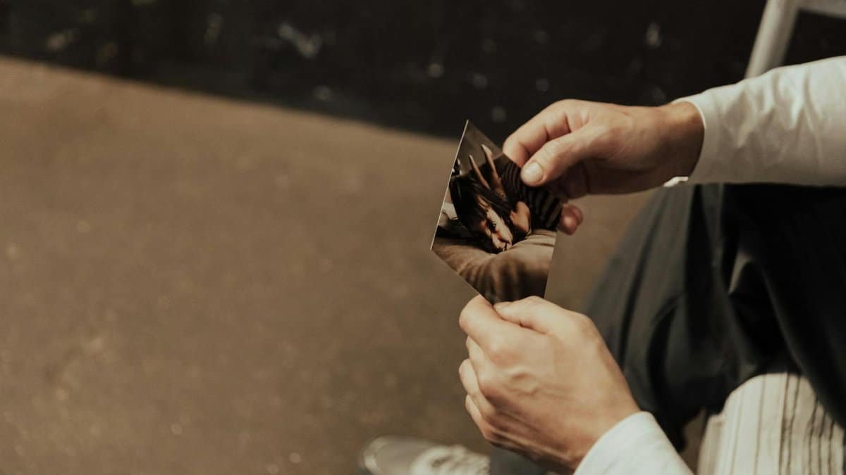 A man reflects on nostalgic memories, holding a cherished photograph indoors.