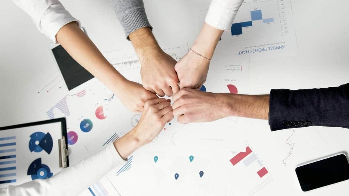 Colleagues celebrate success with a fist bump over financial charts depicting teamwork and unity.