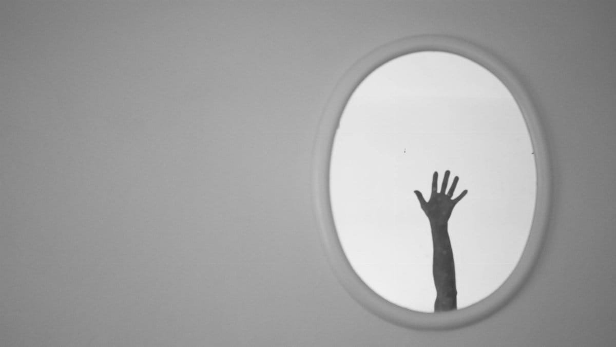 A monochrome image showcasing a hand reaching up in an oval mirror, casting a reflective silhouette.
