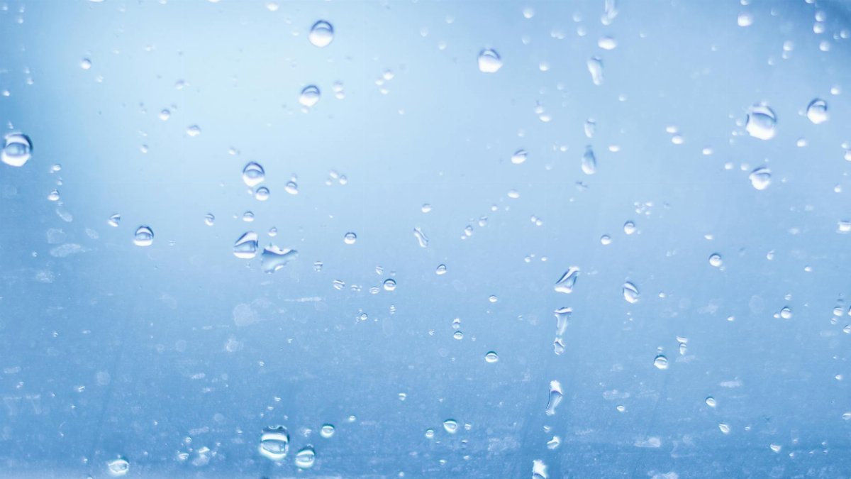 Close-up of raindrops on a clear glass surface, creating a calm abstract pattern.