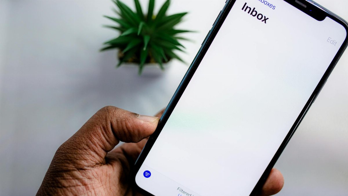 A close-up view of a smartphone screen displaying the email inbox, held by an adult's hand.