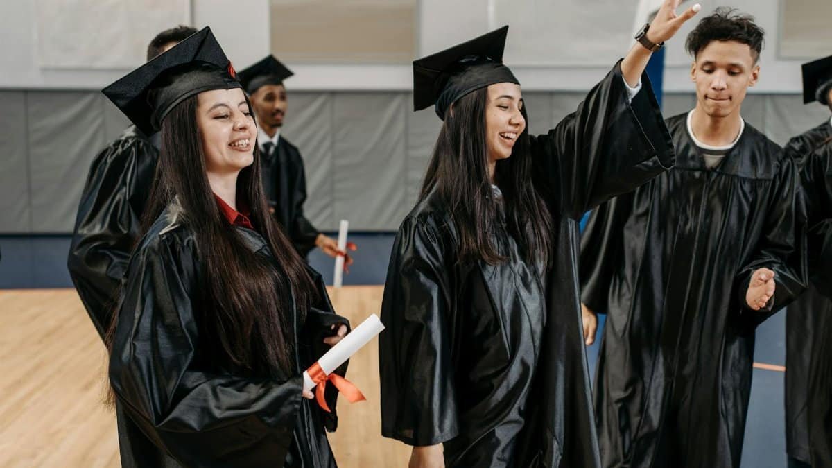 Group of graduates celebrating in caps and gowns indoors, expressing happiness and achievement.