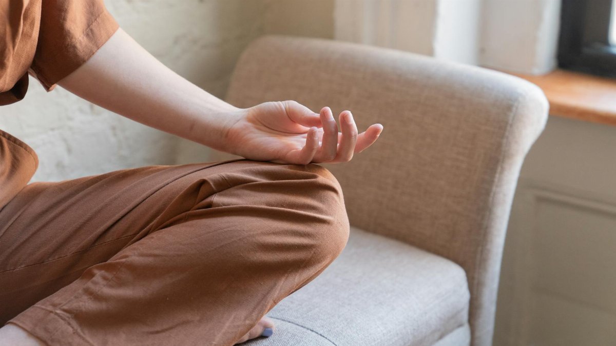 Close-up of a person meditating indoors on a comfortable armchair.